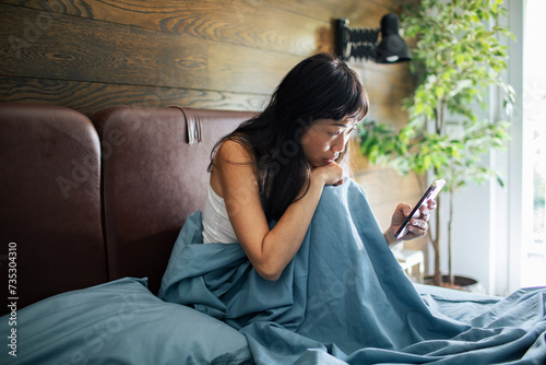 Asian woman using smartphone in bed at home photo