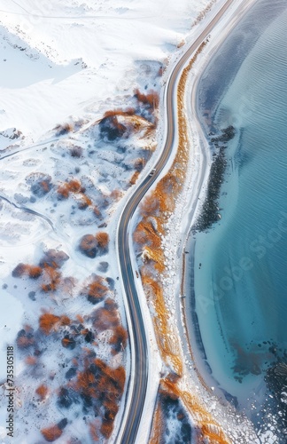 an aerial view of a road next to a body of water with snow on the ground and trees on the other side of the road. photo