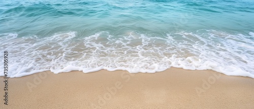 a sandy beach next to the ocean with a wave coming towards the shore and a blue sky in the background.