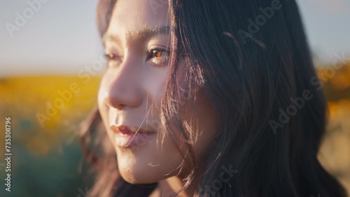 Closeup face of Asian woman opening eyes on sunset background. Young female looking straight at the sunflower field landscape. photo