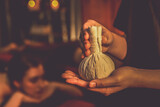 Hot herbal ball spa massage body treatment with masseur's hand hold or show herb bag at spa. Tranquil and serenity of aromatherapy recreation in warm lighting of candles at spa salon. Quiescent