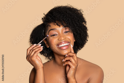 Happy african american woman applying eyeshadow, doing nude makeup