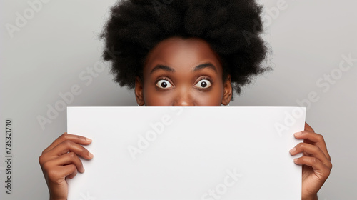 Mulher afro-americana surpresa espiando por trás de um outdoor em branco photo