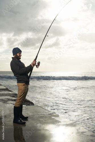 Fishing, holiday and travel with man at beach for adventure, relax and hobby break. Sunset, calm and patience with male fisherman and casting rod pole in nature for recreation, view and vacation
