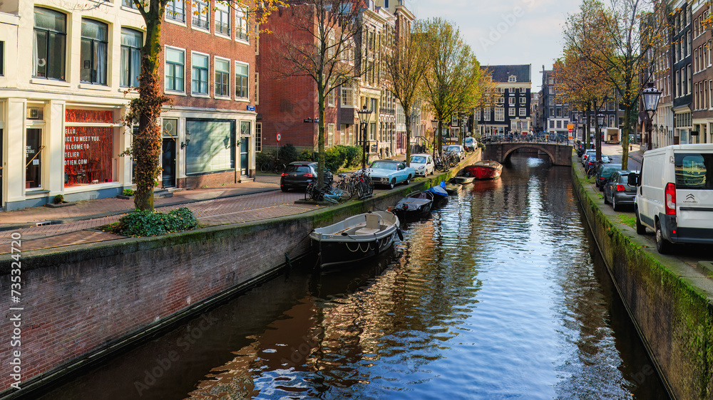 Famous  Amsterdam city center canal  with dutch brick buildings, trees , reflections  and  anchored boats in sunny autumn day. Nedherlands. 