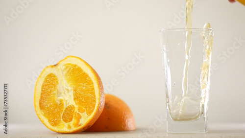 Fototapeta Naklejka Na Ścianę i Meble -  Detail Shot of Pouring Fresh Orange Juice into Glass. Appetizing orange juice swirls into a wave in a glass against the background of cut oranges.