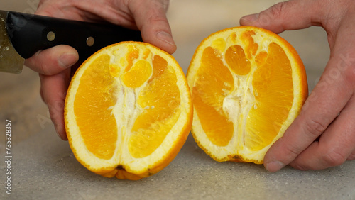Man is cutting fresh juicy orange on two halves. using knife, hands closeup view. Preparing oranges for making juice. Organic fruit