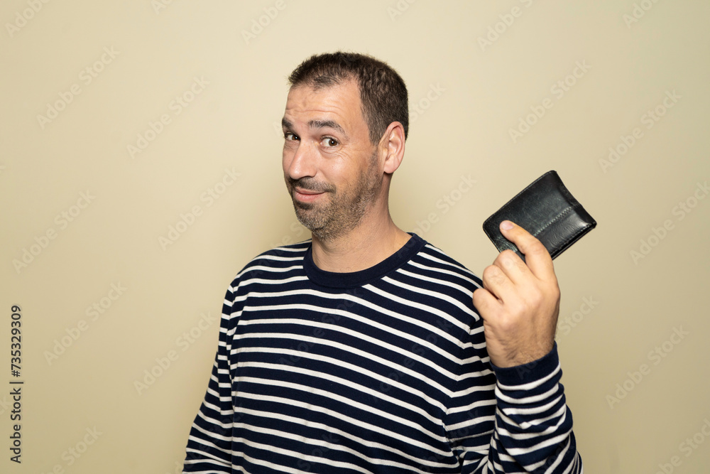 Hispanic man with beard in his 40s wearing a striped sweater smiling and proudly showing his wallet isolated on beige studio background Hispanic man with beard in his 40s wearing a striped sweater smiling and proudly showing his wallet isolated on beige studio background