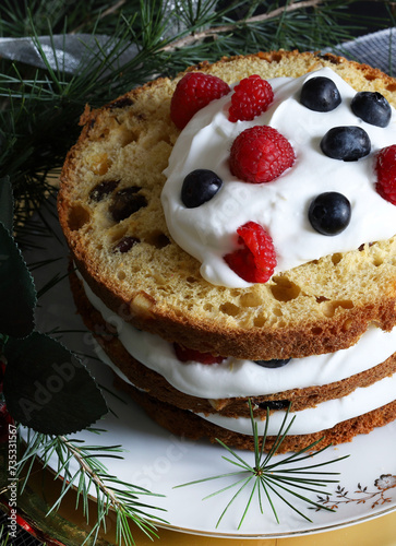 Tradizionale pandoro o panettone natalizio italiano con panna e frutti di bosco su sfondo scuro con decorazioni natalizie. Concetto di tradizioni di Natale e Capodanno.
