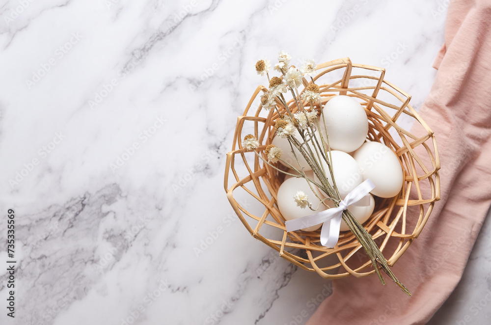 Easter eggs in a basket on a white marble background with a pink napkin and copy space.