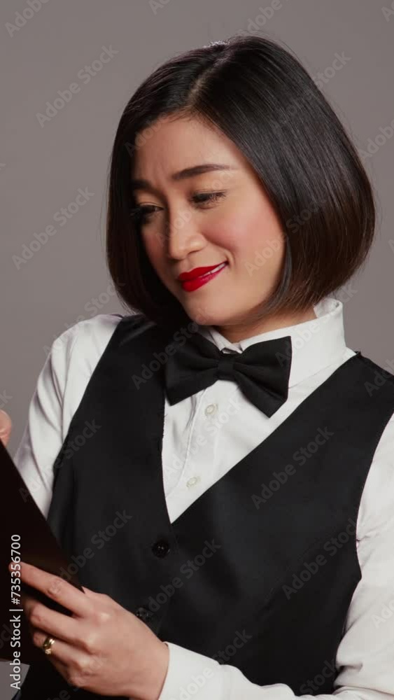 Vertical Video Hospitality industry worker making a list of reservations at hotel, ensuring bookings with clipboard papers in studio. Asian concierge employee checking all guests information. Camera B Vertical Video Hospitality industry worker making a list of reservations at hotel, ensuring bookings with clipboard papers in studio. Asian concierge employee checking all guests information. Camera B