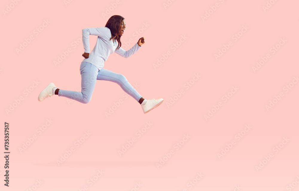 Funny afican american girl wearing casual clothes jumping high isolated on a pink background. Portrait of a happy young excited woman in a hurry having fun in studio. People emotions concept.