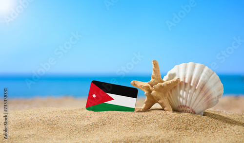 Tropical beach with seashells and Jordan flag. The concept of a paradise vacation on the beaches of Jordan.