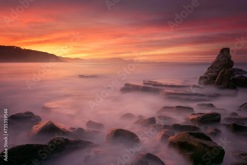 Sunset on Azkorri beach, Getxo with the wakes of the waves between the rocks in the foreground © patxi