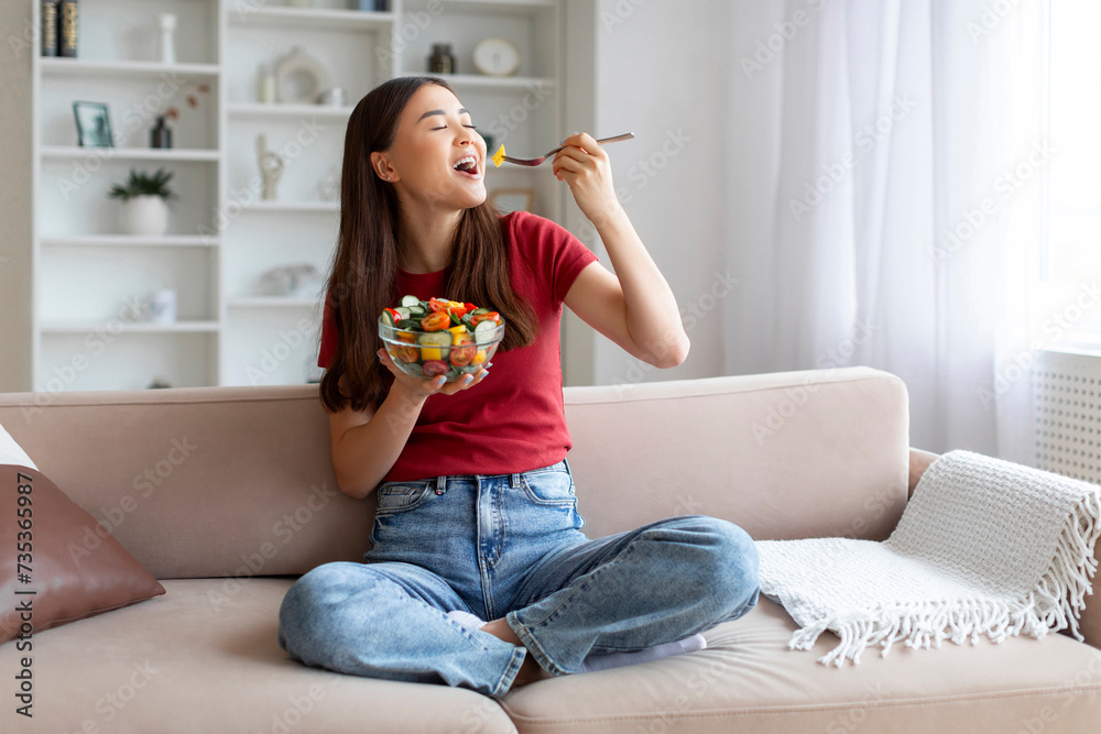 © Prostock-studio - Happy young asian woman enjoying fresh salad bowl at home