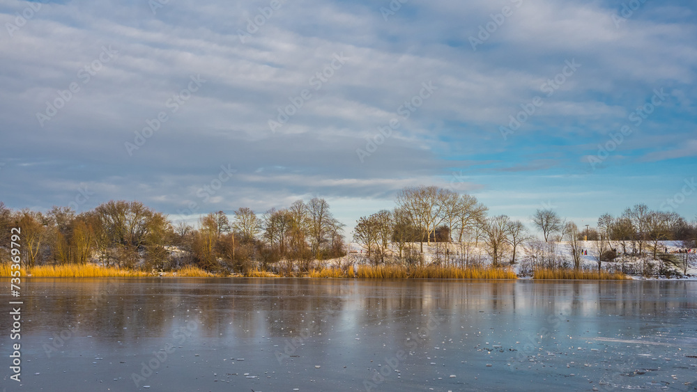 Winter landscape by frozen lake with trees on a snowy shore