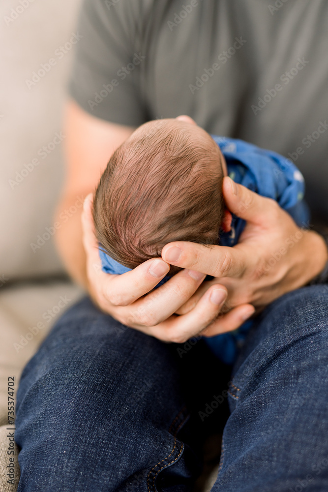 A father holds his newborn son in his arms. The Caucasian baby has a head full of dark hair. A father holds his newborn son in his arms. The Caucasian baby has a head full of dark hair.