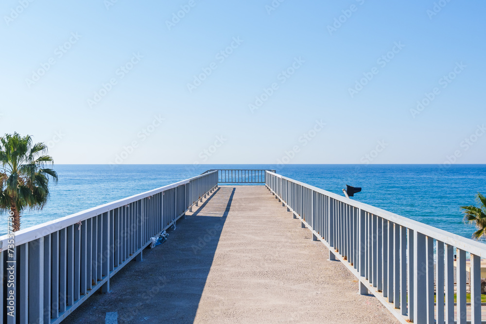 Empty Stone Pedestrian Crosswalk Bridge Over a Highway with a Blue sea and Palm Trees Behind it Under the Clear Sky in a Hot Summer Day