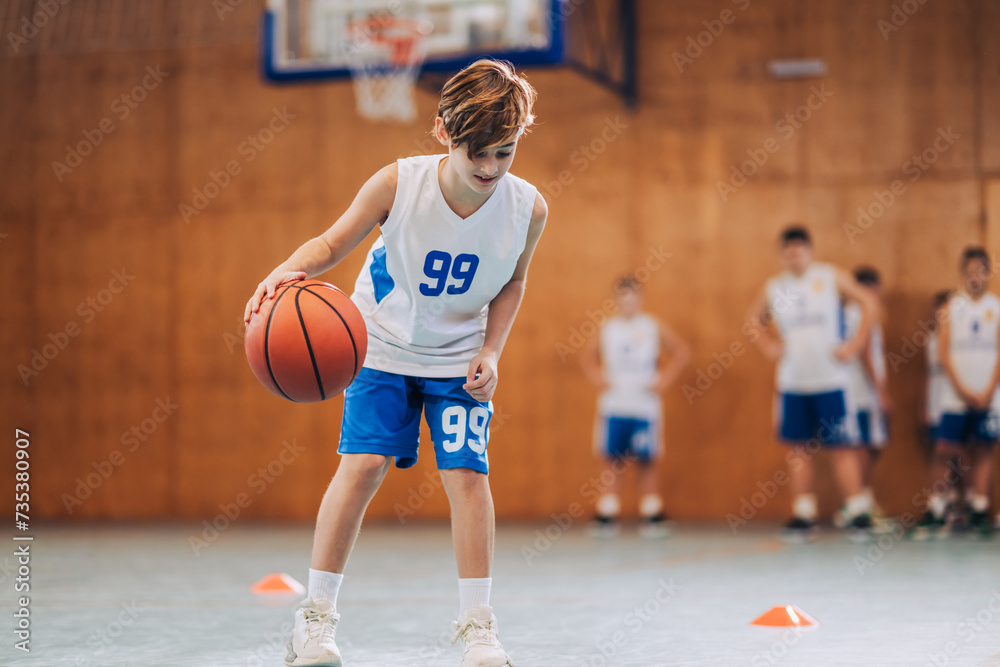 A junior athlete is practicing basketball on training at indoor court.