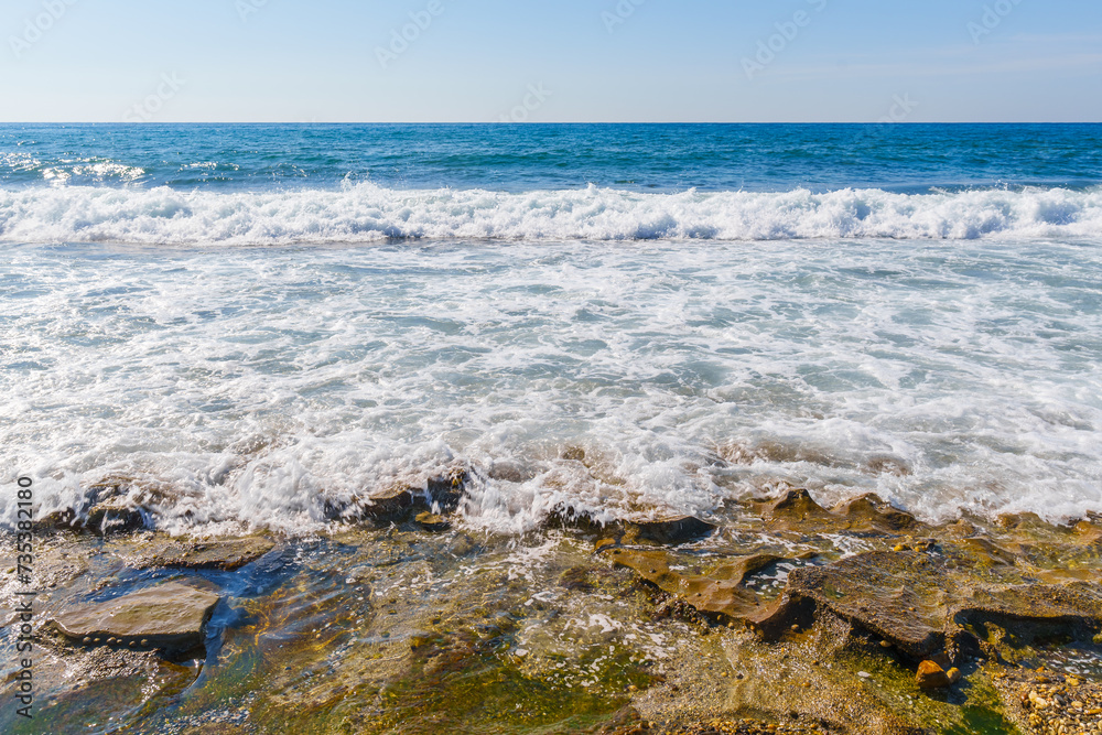 Blue Clear Sea Waves Splashing on a Rocky Beach during a Windy Day With Clear Blue sky