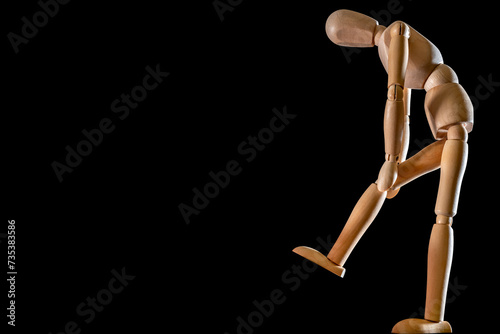 Hölzerne Figur vor schwarzem Hintergrund hält sich das Kniegelenk zum Thema Knieschmerzen photo