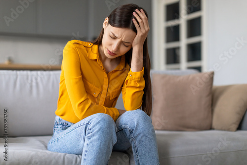 Obraz na plátně Stressed young woman with headache sitting on the couch