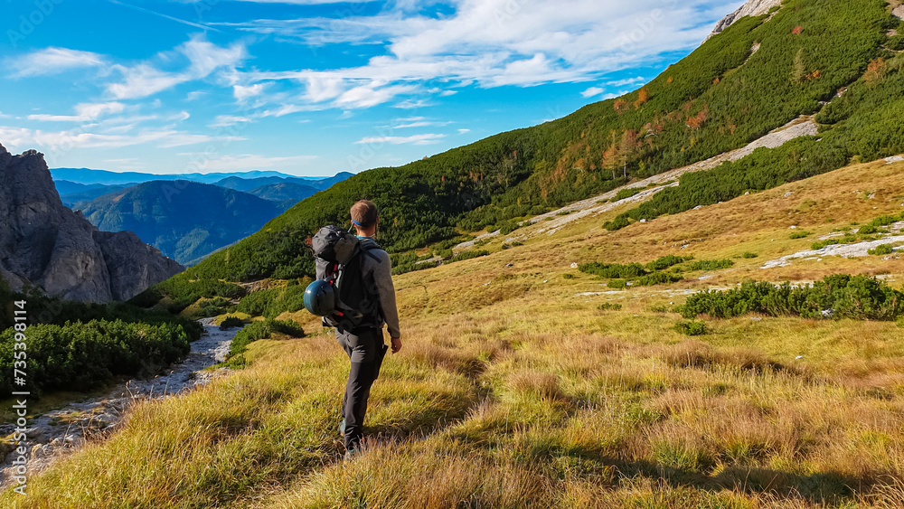 Hiker man on golden alpine meadow with scenic view of Hochschwab mountain range, Styria, Austria. Hiking trail in alpine terrain. Remote Austrian Alps in summer. Escapism. Connect with nature