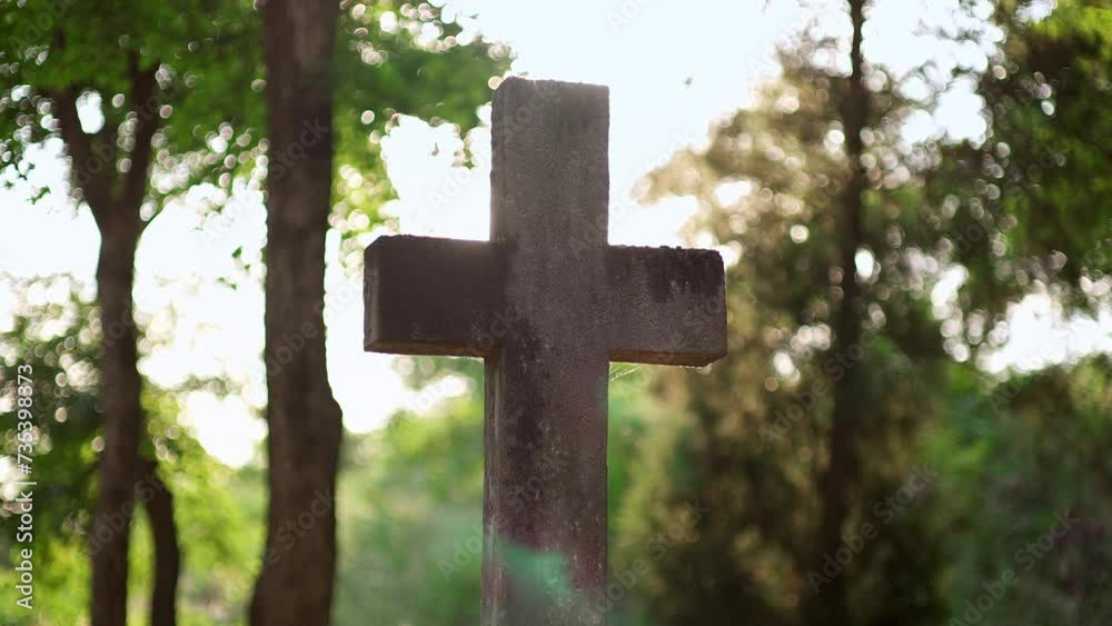 ancient stone cross covered in moss stands in a cemetery with sunlight shine in camera. The mystical graveyard is filled with numerous graves, especially enchanting during sunrise or sunset. ancient stone cross covered in moss stands in a cemetery with sunlight shine in camera. The mystical graveyard is filled with numerous graves, especially enchanting during sunrise or sunset.