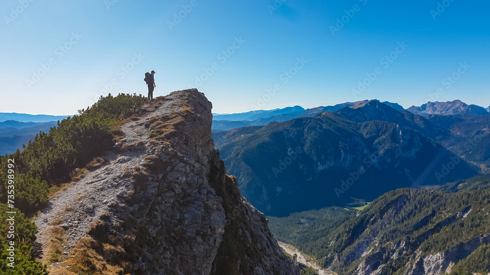 Hiker man standing on mountain summit with panoramic view of majestic Hochschwab massif, Styria, Austria. Idyllic hiking trail in remote Austrian Alps. Sense of escapism, peace, personal reflection