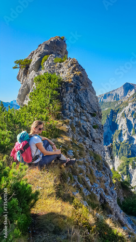 Hiker woman resting next to unique rock formation with panoramic view of majestic Hochschwab massif, Styria, Austria. Idyllic hiking trail in remote Austrian Alps. Sense of escapism, peace, reflection photo
