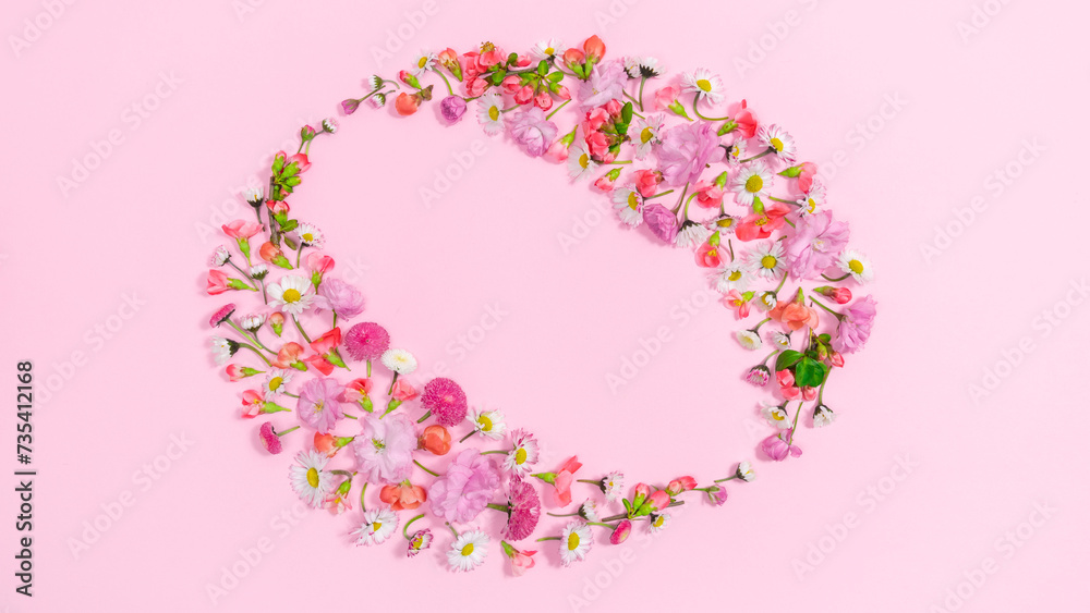 Heads of natural fresh flowers form an oval frame. Pink background.