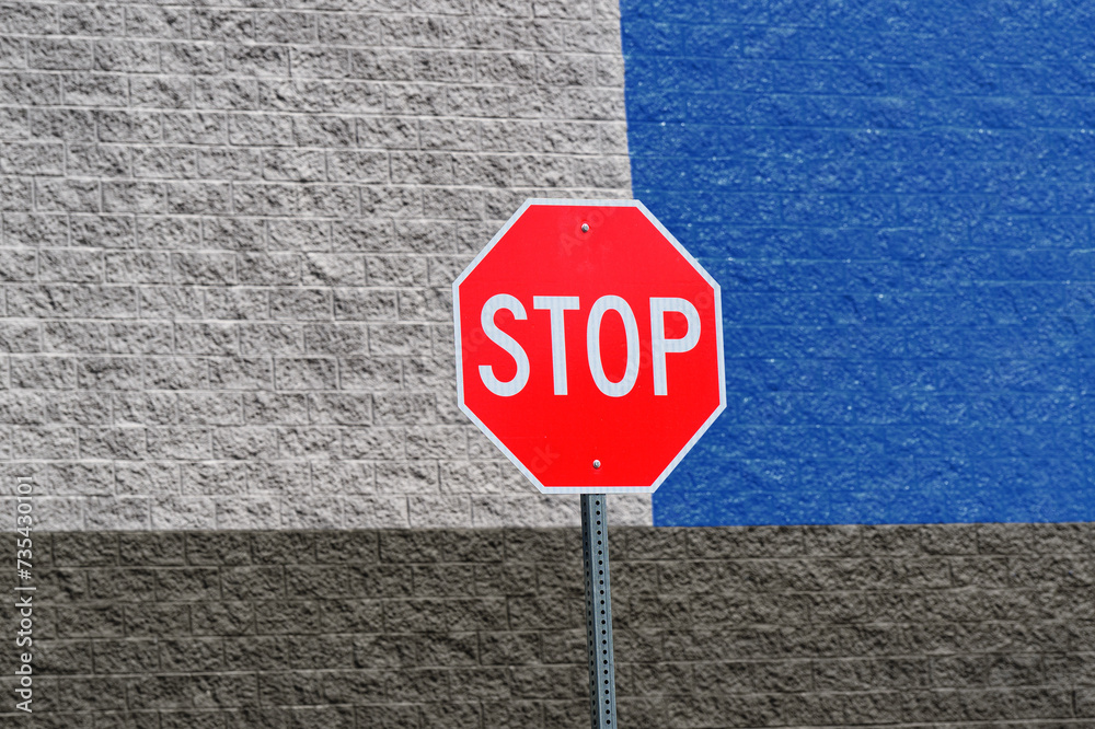 A stop sign in front of a stone wall in Upstate NY. The contrast of the red sign is accentuated and intensified by the 3 color, white, grey and blue, behind it. Bright image of sign and building. A stop sign in front of a stone wall in Upstate NY. The contrast of the red sign is accentuated and intensified by the 3 color, white, grey and blue, behind it. Bright image of sign and building.