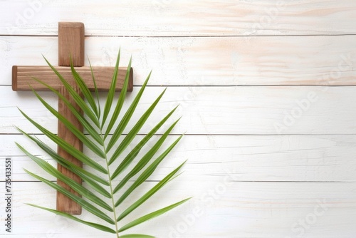 A cross and a palm leaf on a white wooden background Palm Sunday, wooden christian cross with palm leaf on textured light background © Friedbert