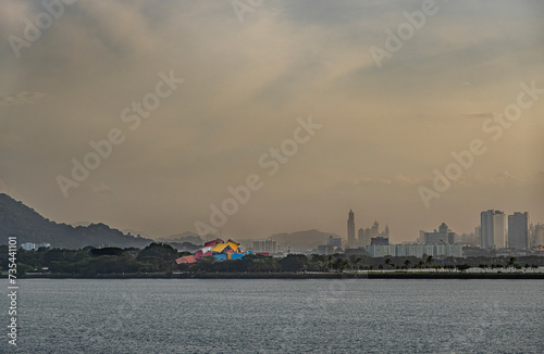 Panama Canal, Panama - July 24, 2023: Colorful biodiversity museum stands out at entrance in foggy morning cloudscape. Cityscape part, green mountain and green tree belt photo