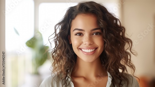 Woman with curly hair smiling in front of a window.