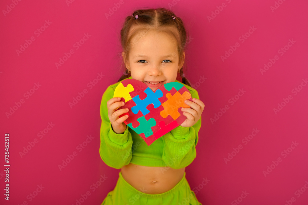 A girl with a heart-shaped postcard decorated with colored puzzles, made in support of autistic people A girl with a heart-shaped postcard decorated with colored puzzles, made in support of autistic people