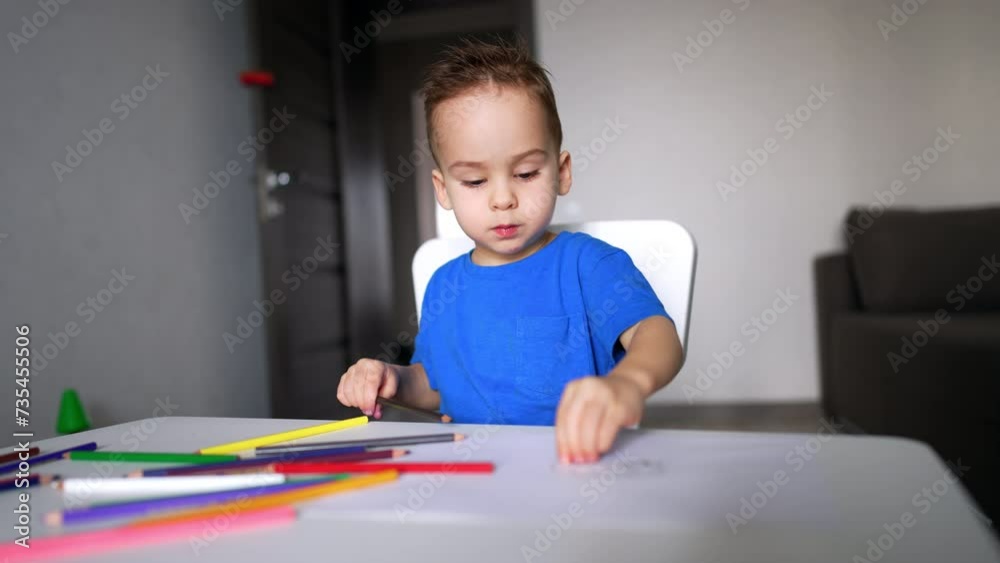 Calm little kid sitting at desk busy with drawing. Toddler pulls the sheet of paper closer holding a brown pencil. Calm little kid sitting at desk busy with drawing. Toddler pulls the sheet of paper closer holding a brown pencil.