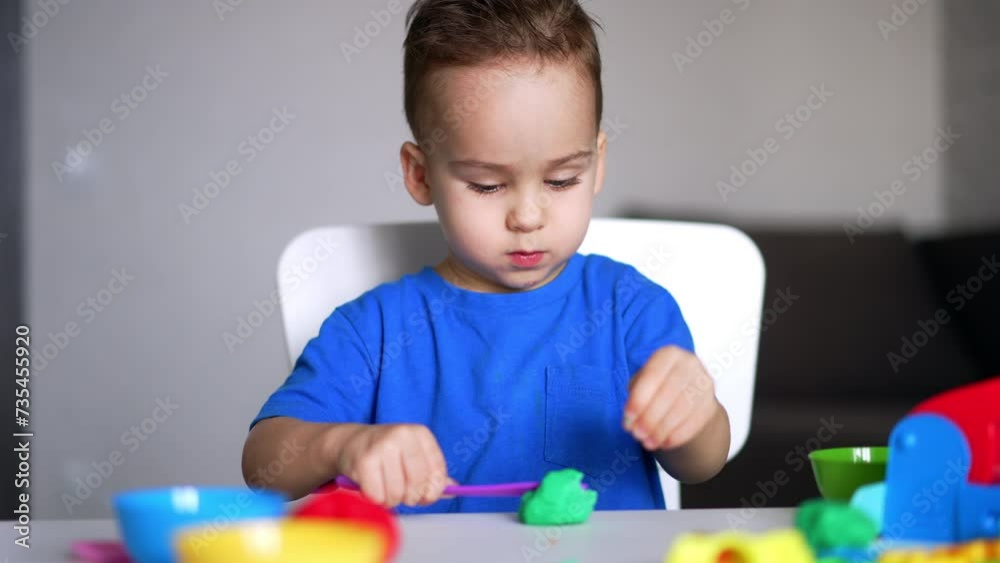 Calm focused baby boy in blue t-shirt playing at desk. Kid cuts the piece of green plasticine with a stick. Calm focused baby boy in blue t-shirt playing at desk. Kid cuts the piece of green plasticine with a stick.