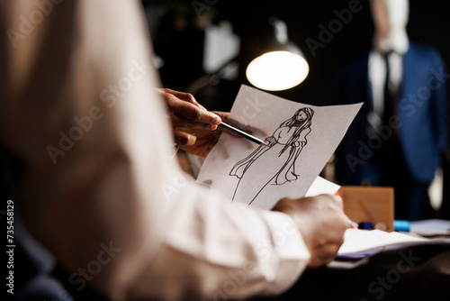 Meticulous expert dressmaker designing comissioned wedding dress for customer in luxury atelier shop. Skilled tailor looking over sketch drawing, planning upcoming adjustments photo