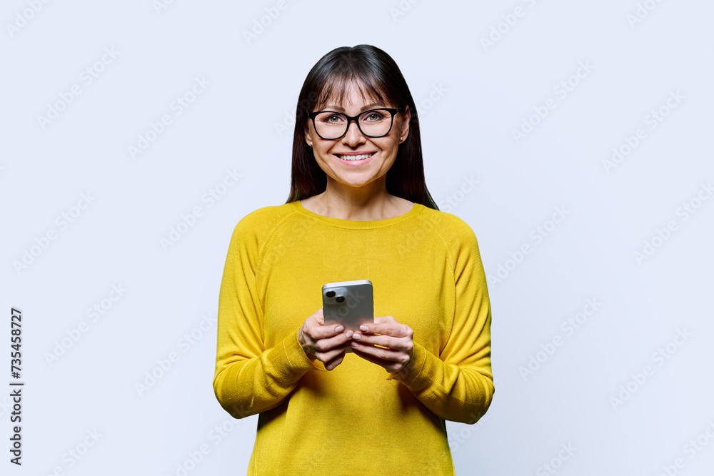 Middle aged smiling woman using smartphone on white studio background