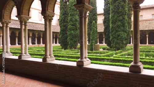 TOULOUSE, FRANCE - MARCH 20 2018: Cloister and French garden with cypress tree and trimmed bushes, in the Dominican Convent of Jacobins, a medieval brick monastery housing Thomas Aquinas burial. photo
