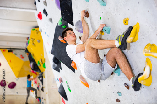 Male alpinist practicing indoor rock-climbing on artificial boulder without safety belts