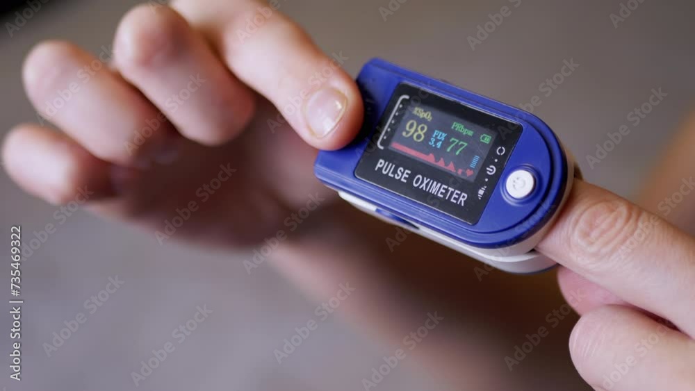 Female Hands Show Measures Pulse and Oxygen Saturation Using a Pulse Oximeter in Room. Close up. Blurred background. Dial with sensors and indicators on the device. Measurement of heart rate, pulse. Female Hands Show Measures Pulse and Oxygen Saturation Using a Pulse Oximeter in Room. Close up. Blurred background. Dial with sensors and indicators on the device. Measurement of heart rate, pulse.