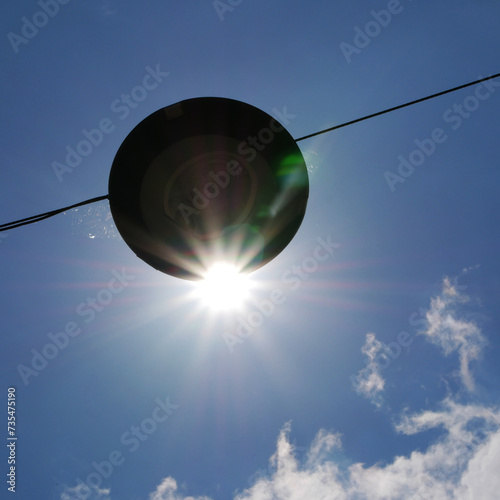disk shaped street light hanging in blue sky © AE & mekke
