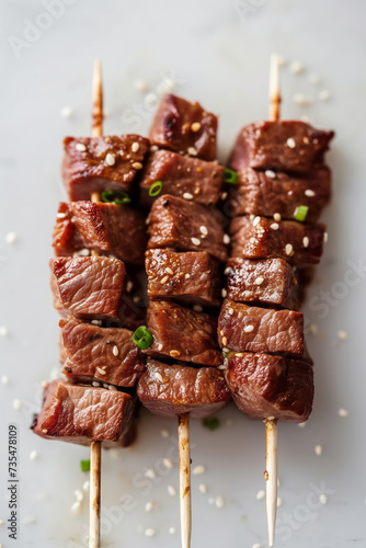 Wagyu meat pieces skewered on bamboo skewers against the light grey background