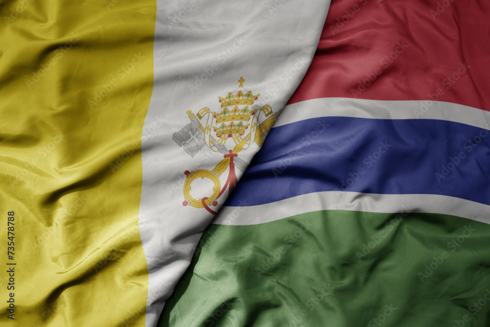 Fototapeta premium big waving national colorful flag of gambia and national flag of vatican city.