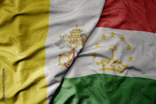 big waving national colorful flag of tajikistan and national flag of vatican city.