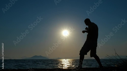 Man silhouette doing shadow boxing. A view of sporty man silhouette practising sport on the empty beach during sunset in summer. photo
