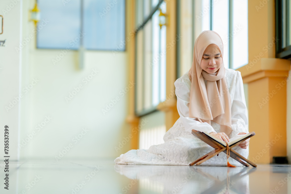 © maya1313 - Ramadan, quran, The image of an Asian Muslim woman in the Islamic religion in hijab in cream color. reading the Quran and having a happy Staying in a beautiful mosque, Arabic word Holy Al Quran.
