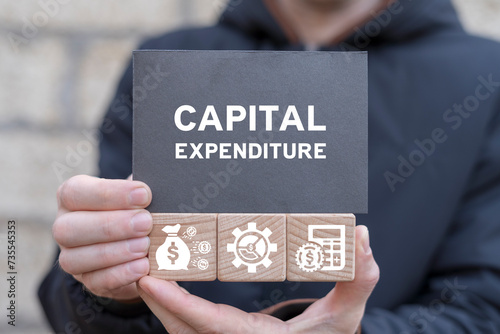 Man holding wooden cubes with icons and black sticky note with text: CAPITAL EXPENDITURE. Capital expenditure business finance concept.